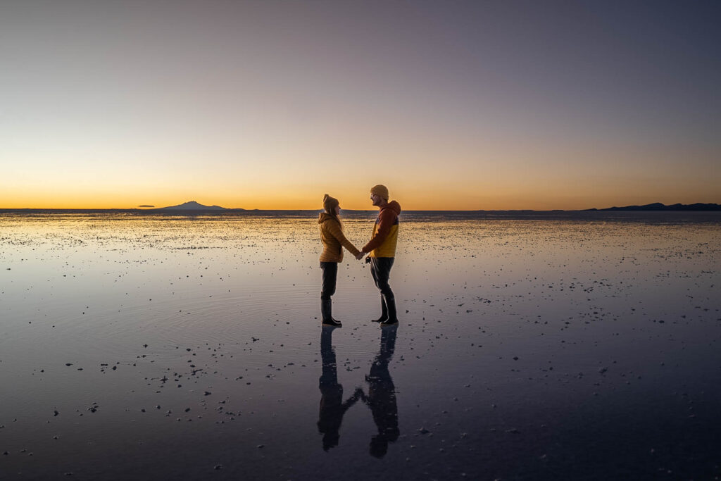 Couple holding hands on the flooded Uyuni Salt Flats at sunset in Bolivia