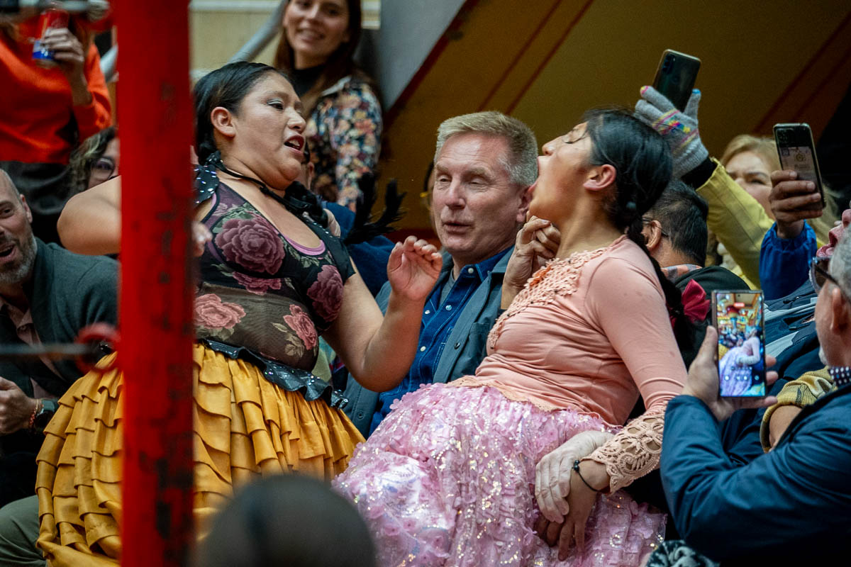 Two cholitas yelling at each other on top of an audience member at a Cholita Wrestling show in La Paz, Bolivia