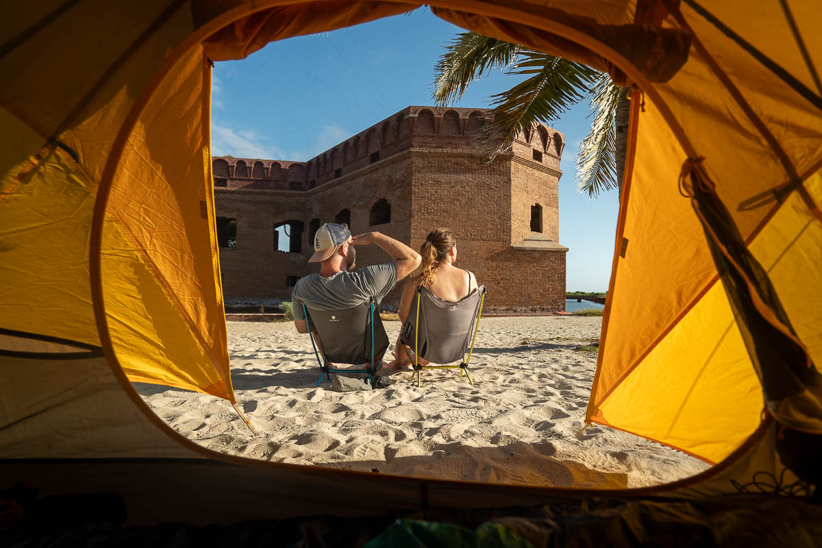 View of couple sitting in camping chairs with Fort Jefferson and a coconut tree in the background in Dry Tortugas National Park in Florida