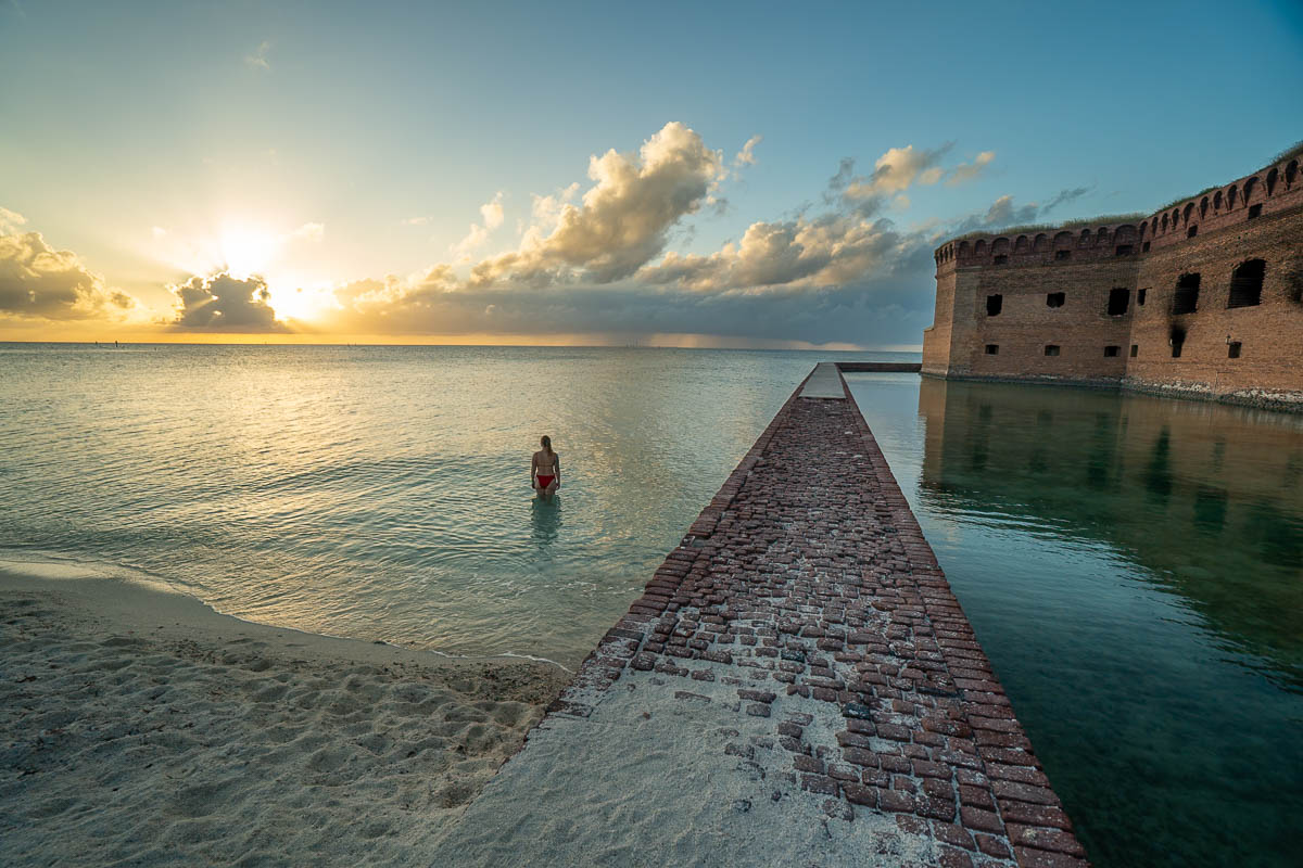 Woman standing in water next to a brick moat wall next to Fort Jefferson at sunset in Dry Tortugas National Park off Florida