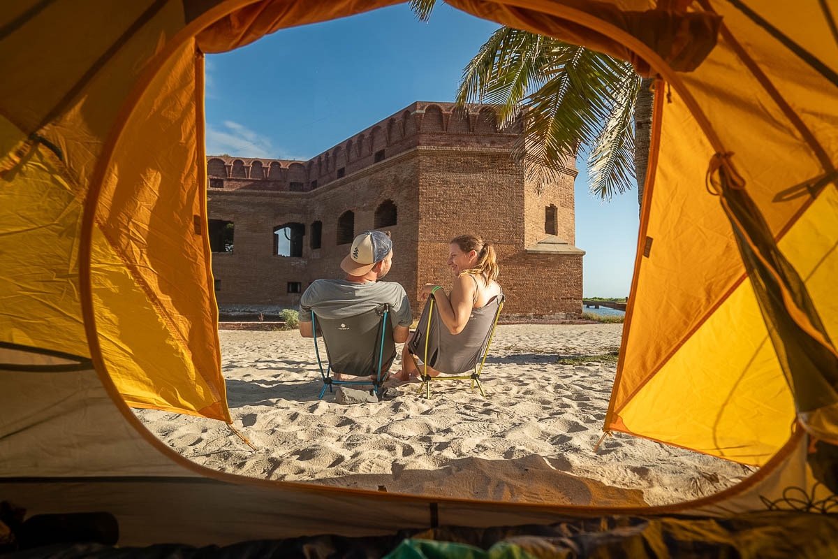 Couple sitting in camping chairs in front of a tent with Fort Jefferson in the background in Dry Tortugas National Park