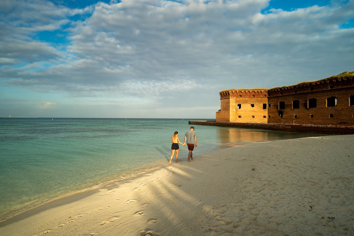 Couple walking on a white sandy beach with Fort Jefferson in the background in Dry Tortugas National Park near Key West, Florida
