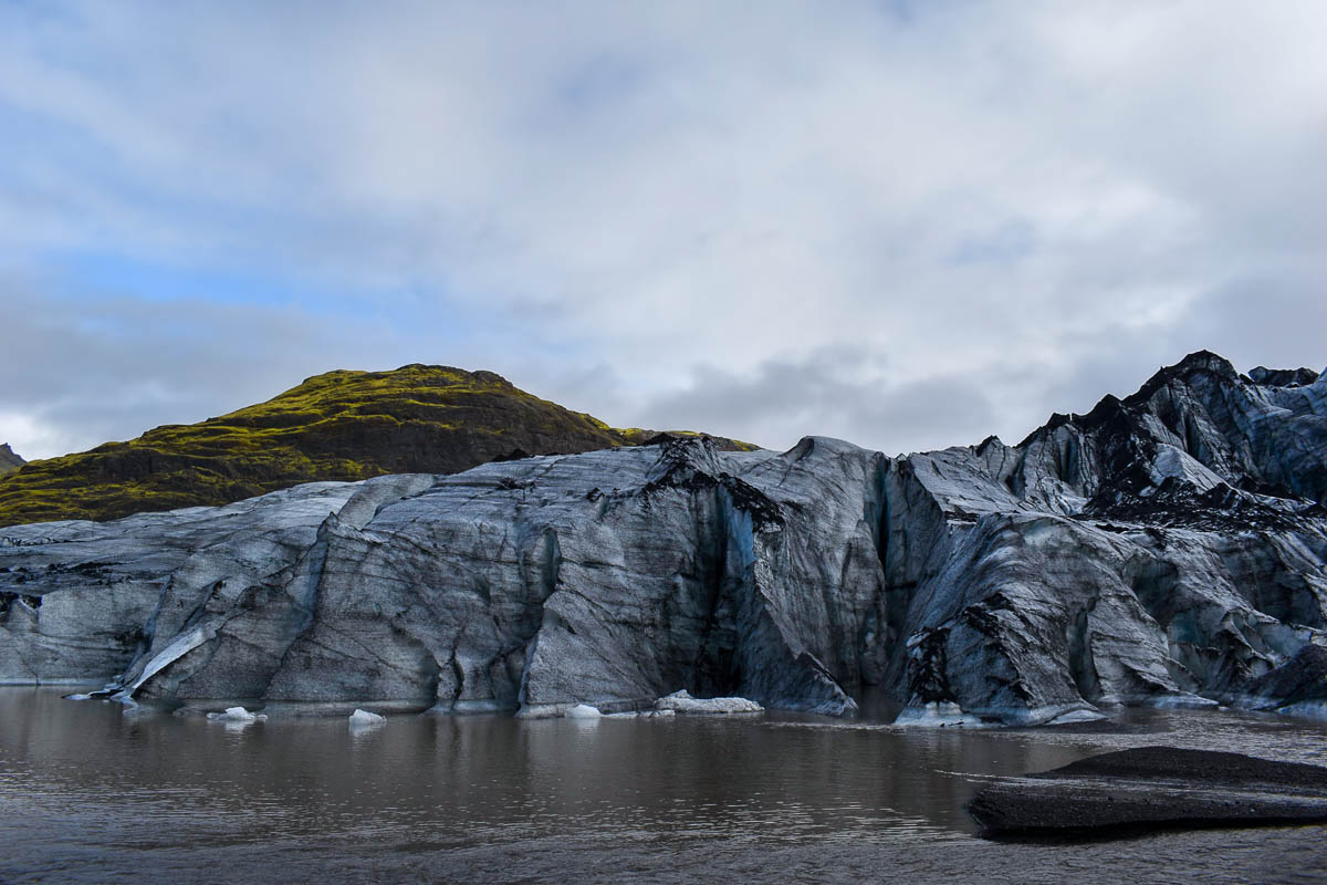 Sólheimajökull Glacier with a glacier lagoon in the foreground and mossy mountains in the background in Iceland