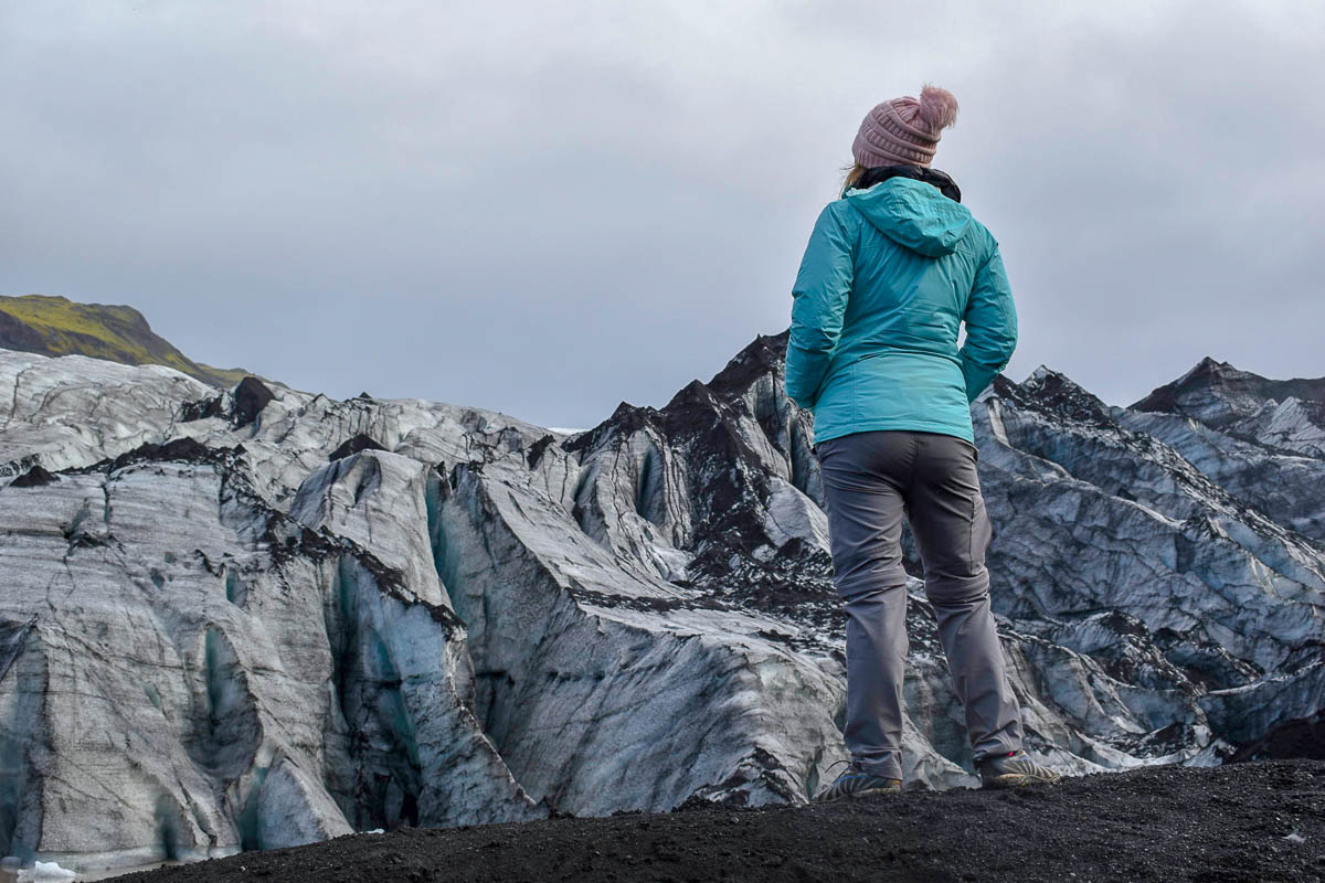 Woman standing on a volcanic sand with Sólheimajökull Glacier in the background in Iceland
