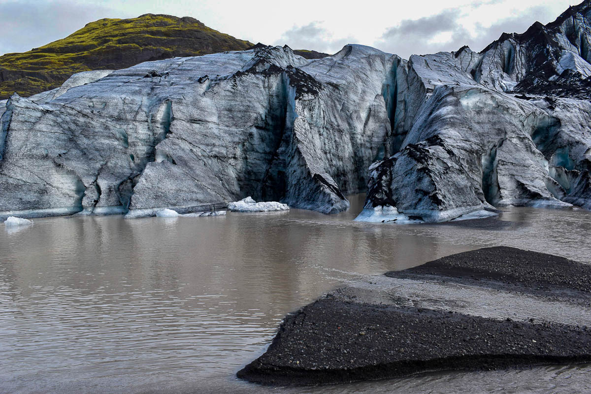 Sólheimajökull Glacier with a glacier lagoon in the foreground and mossy mountains in the background in Iceland