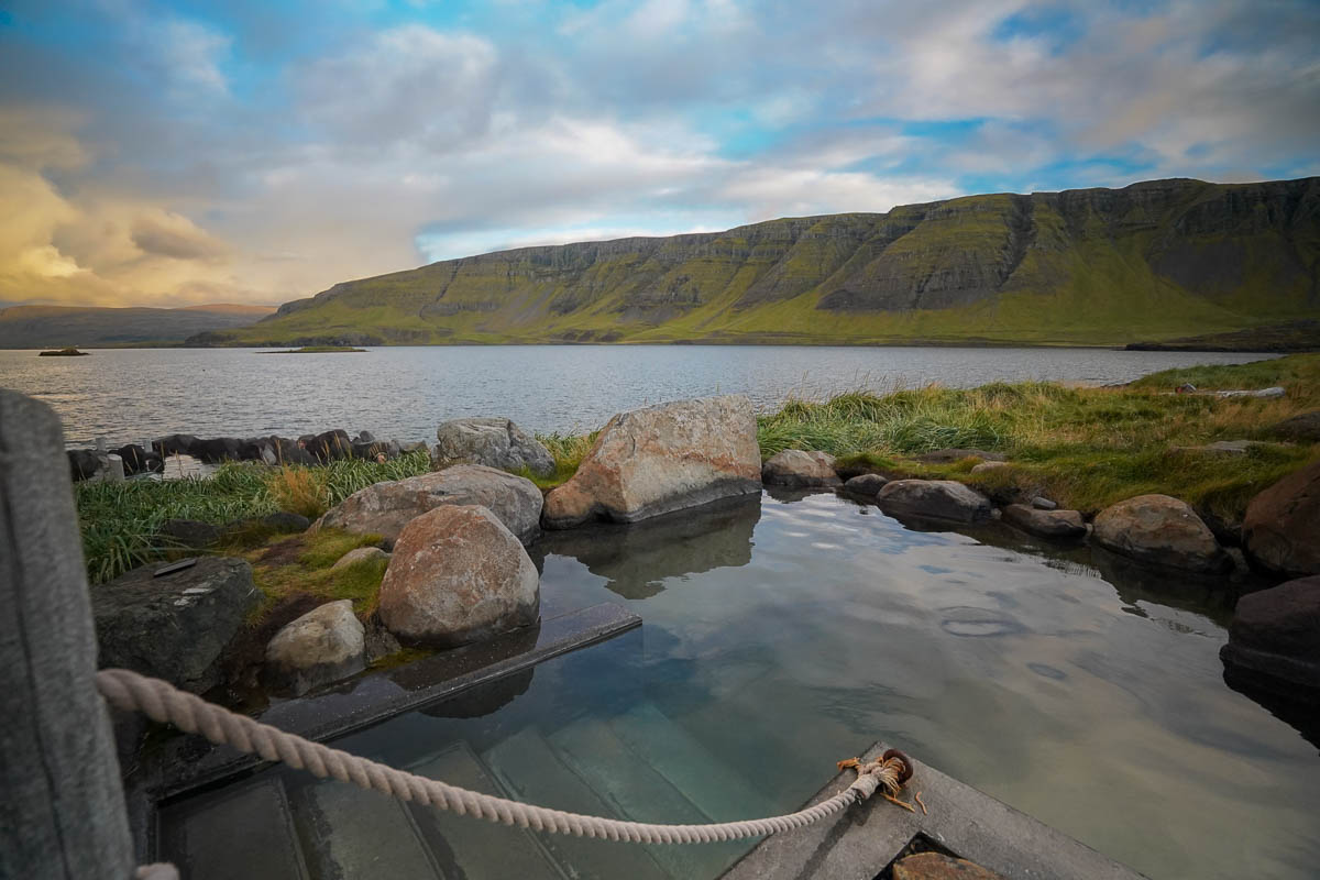 Pool along the shores of Hvalfjörður with green mountains in the background at Hvammsvik Hot Springs in Iceland