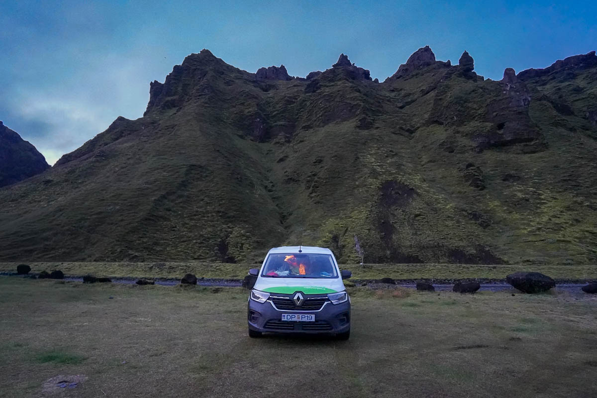 Happy Campers campervan parked in front of green rugged mountains in the Pakgil Campground in Iceland