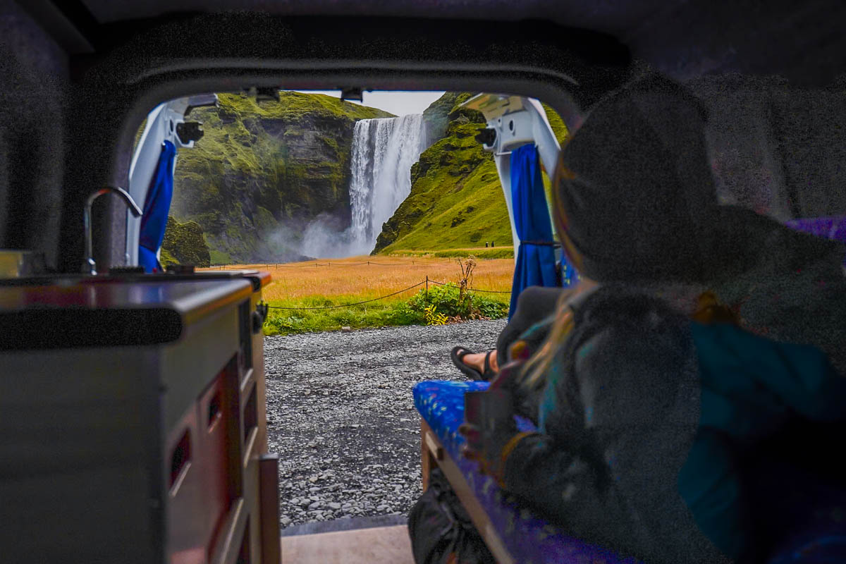 Woman lying down in the back of a campervan looking at the Skogafoss Waterfall in Iceland