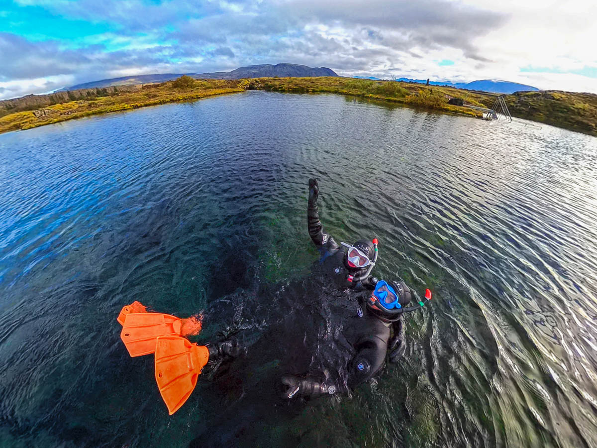 Couple floating on their backs in Silfra Lagoon wearing drysuit and snorkeling gear in Silfra in Iceland
