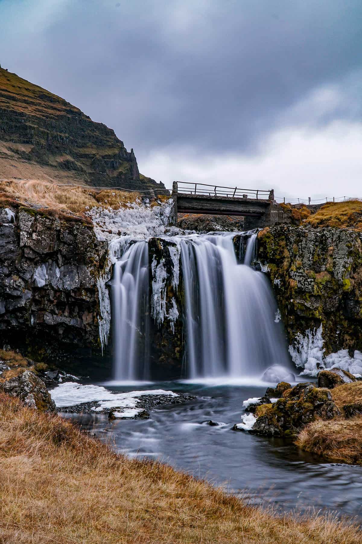 Wooden bridge over the Kirkjufellsfoss waterfall surrounded by mossy cliff sides in Iceland