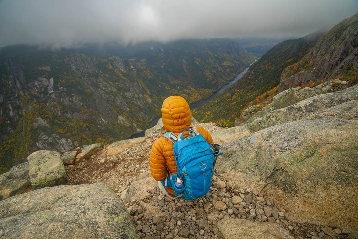 Woman sitting on a rocky outcropping at the summit of Acropole des Draveurs in the Hautes‑Gorges-de-la-Rivière‑Malbaie National Park in Quebec, Canada
