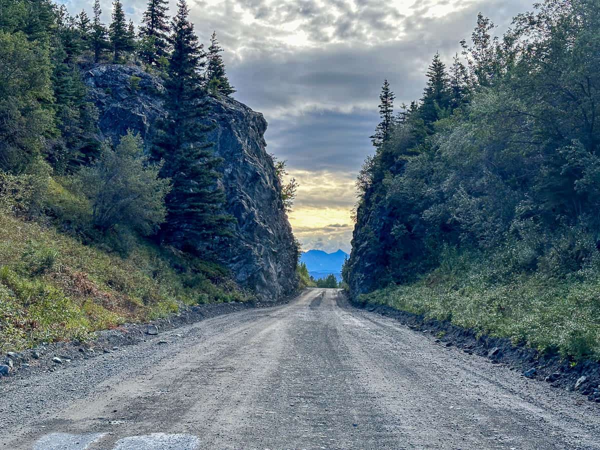 McCarthy Road leading between narrow rocky cliffs with pine trees heading to McCarthy, Alaska