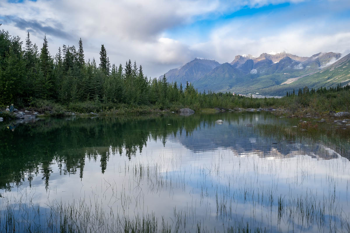 Lake along McCarthy Road with pine trees and mountains in the background in McCarthy, Alaska