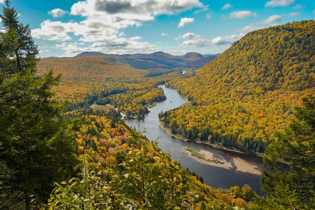 View of Rivière Jacques-Cartier surrounded by hillsides covered with fall foliage along the L'Eperon Trail at Jacques Cartier National Park in Quebec, Canada
