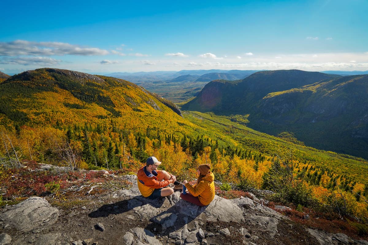 Couple sitting at a rocky outcropping at Mont St. Michel with fall foliage across hillsides along the Mont du Dome trail in Quebec, Canada
