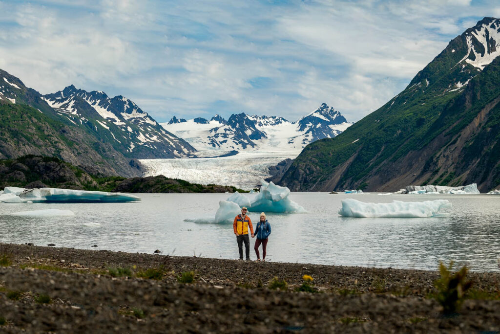 Couple standing in front of icebergs in the Grewingk Glacier lake in Kachemak Bay State Park in Alaska