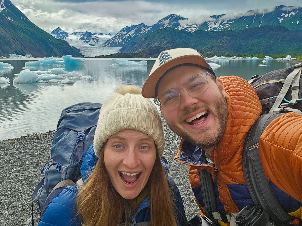 Couple smiling in front of icebergs in the Grewingk Glacier Lake with mountains in the background in Kachemak Bay State Park in Alaska