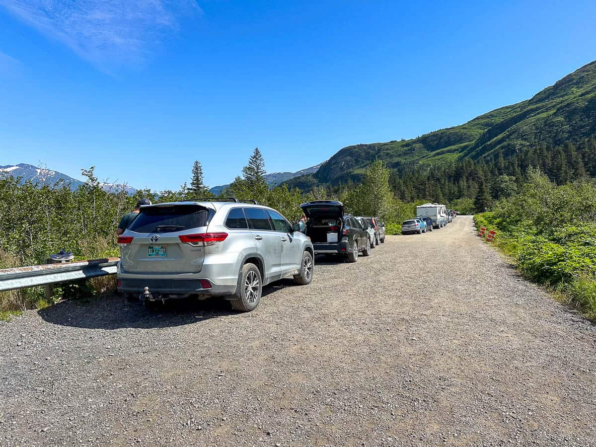 Cars parked along a gravel road at the Portage Pass trailhead with mountains in the background in Whittier, Alaska