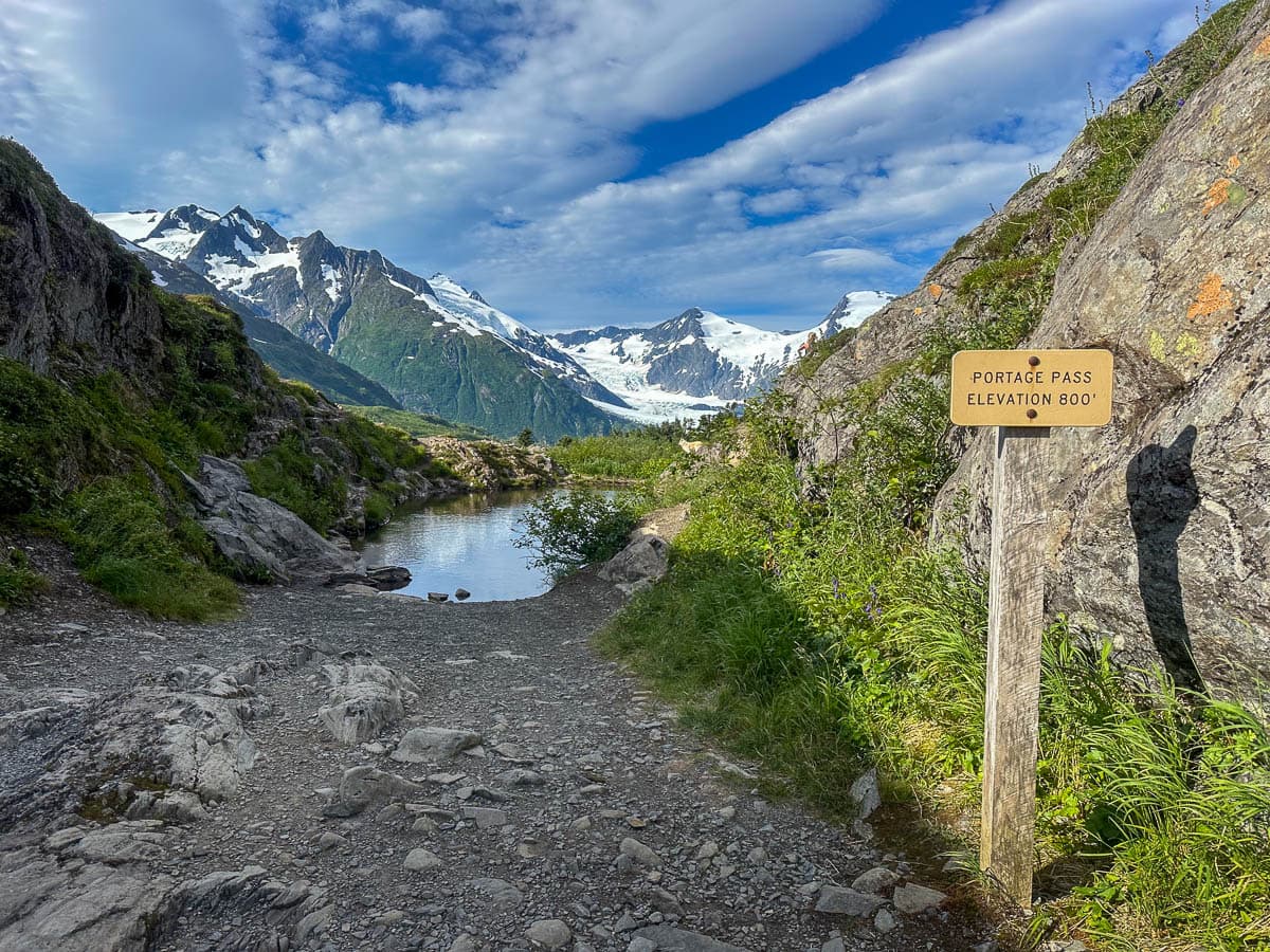 Sign for Portage Pass with mountains and the Portage Glacier in the background along Portage Pass Trail in Whittier, Alaska