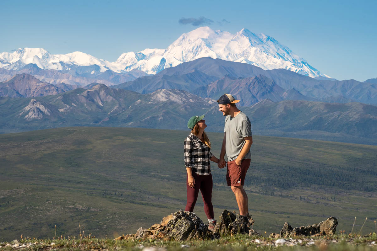 Couple holding hands with Mount Denali and the Alaska Mountain range in the background along the Savage Alpine Trail in Denali National Park, Alaska