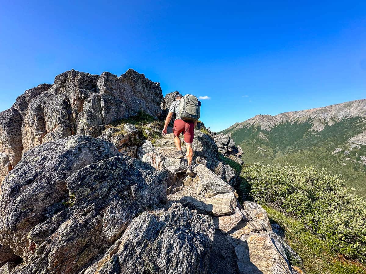 Man climbing up a rock formation along the Savage Alpine Trail in Denali National Park, Alaska