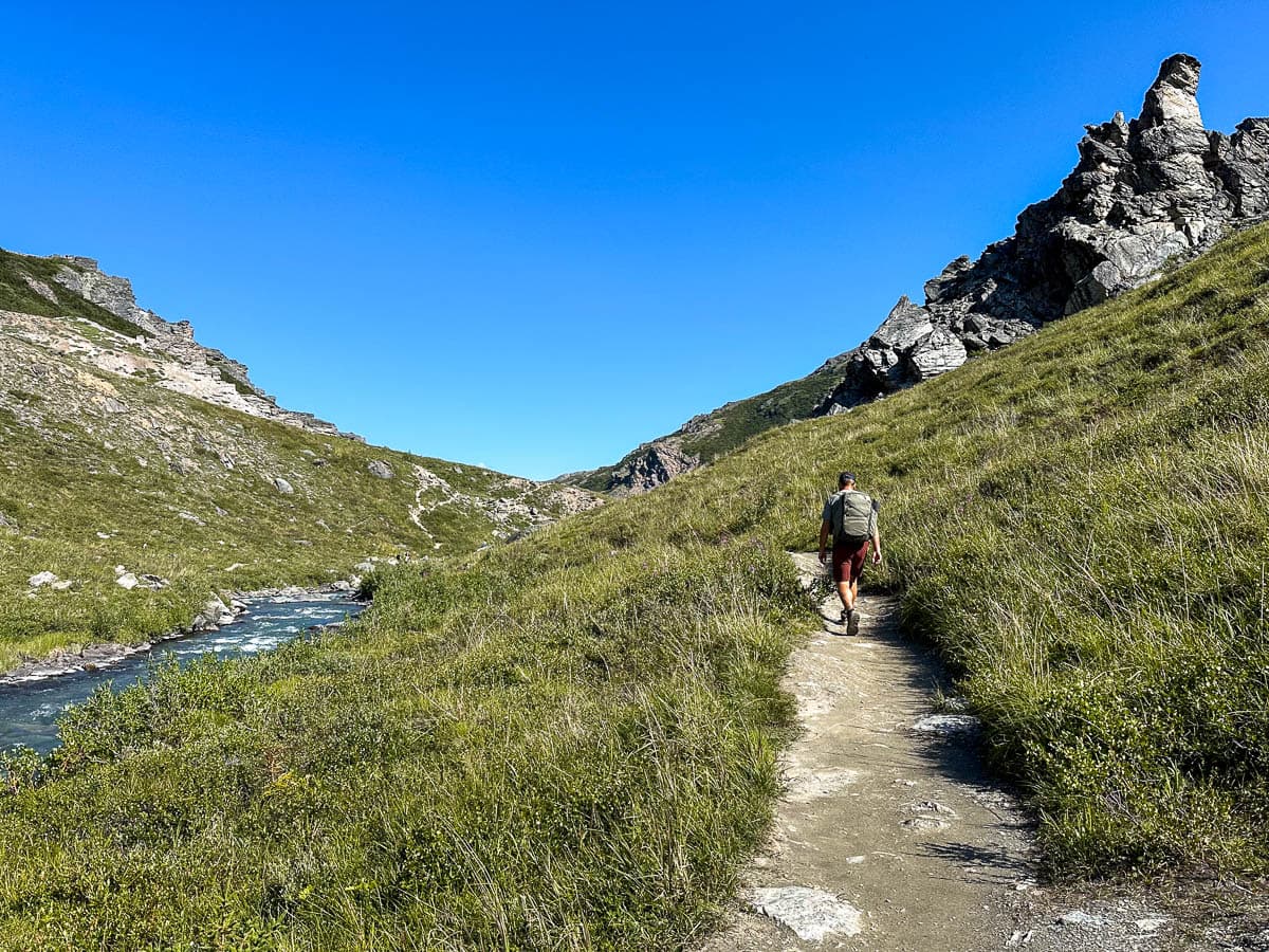 Man hiking along the Savage River with a mountain slope with rugged rock formations along the Savage River Loop Trail in Denali National Park, Alaska