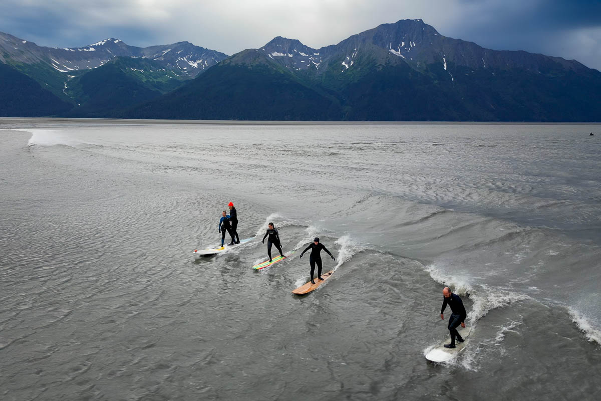 People surfing on the bore tide in the Turnagain Arm with the Kenai Mountains in the background near Anchorage, Alaska