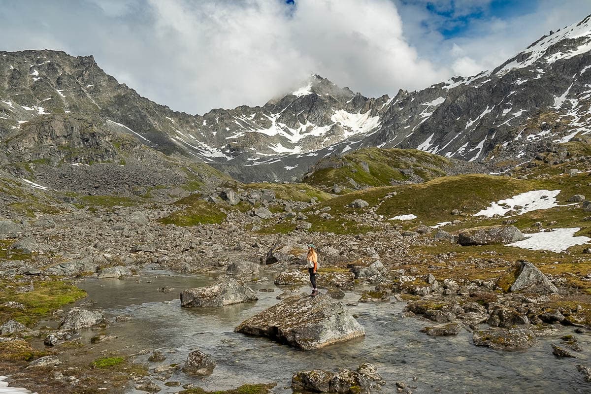 Woman standing on a rock along a stream along the Reed Lakes Trail in Hatcher Pass, Alaska