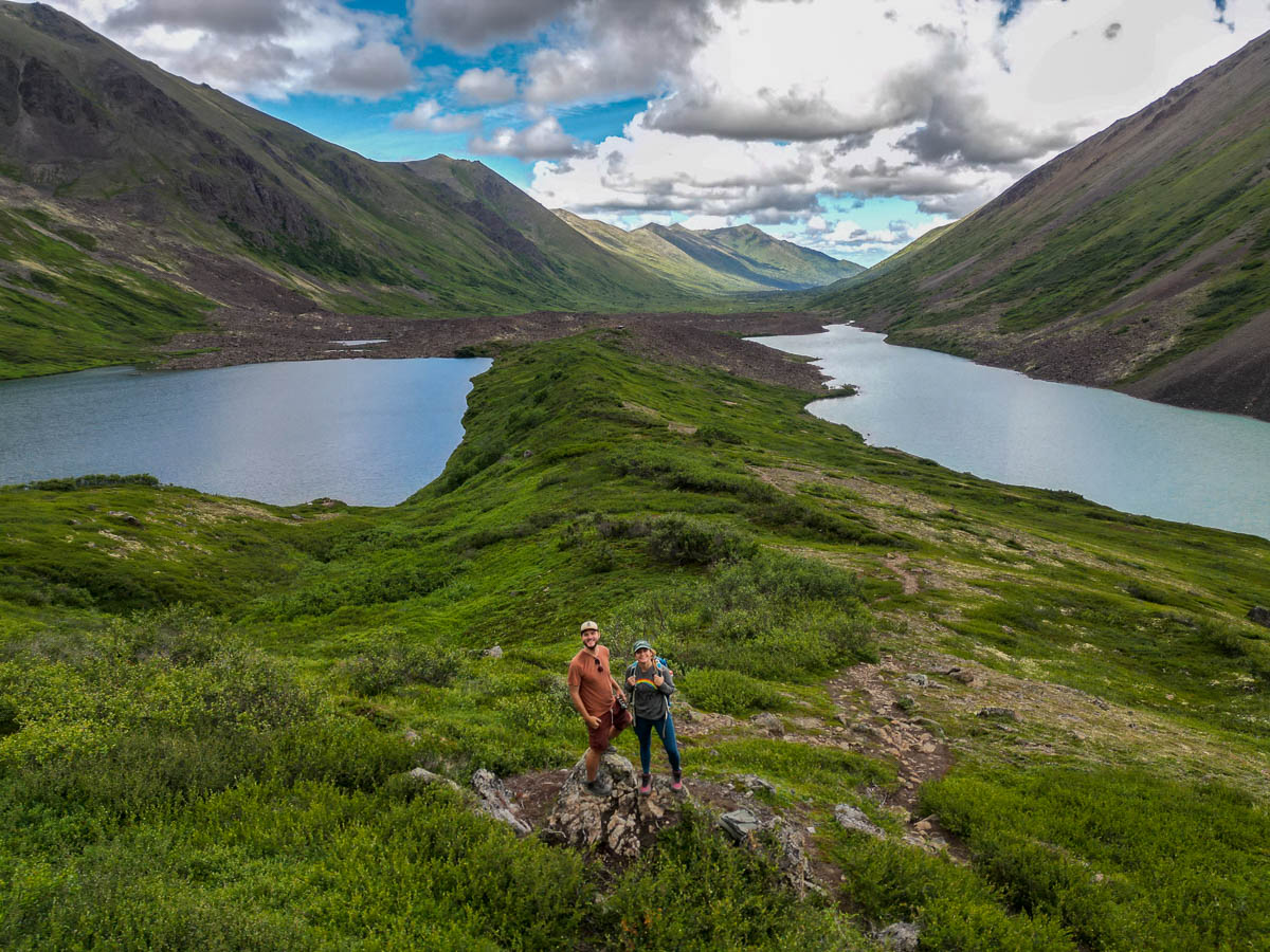 Couple standing on a rocky outcropping with Eagle and Symphony Lakes in the background along the South Fork Valley Trail in Chugach State Park in Anchorage, Alaska