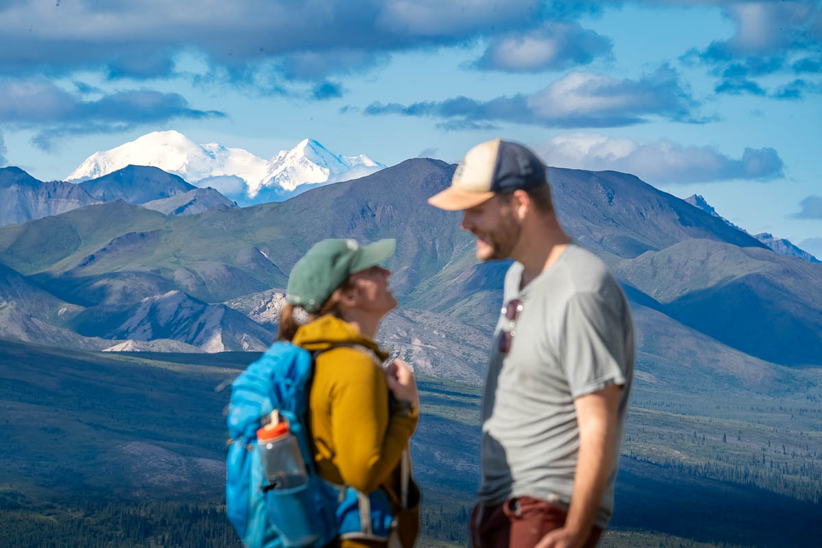 Couple smiling at each with Mount Denali peeking out from the Alaska Mountain range along the Mount Healy Overlook Trail in Denali National Park, Alaska