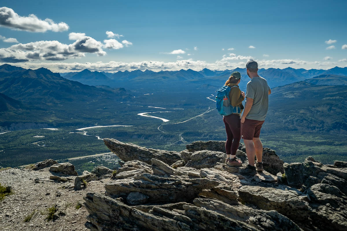Couple standing on a rocky outcropping with the Alaska Mountain range in the background along the Mount Healy Overlook Trail in Denali National Park, Alaska