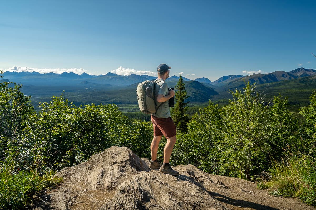 Man standing on a rocky outcropping with the Alaska Mountain range in the background along the Mount Healy Overlook Trail in Denali National Park, Alaska