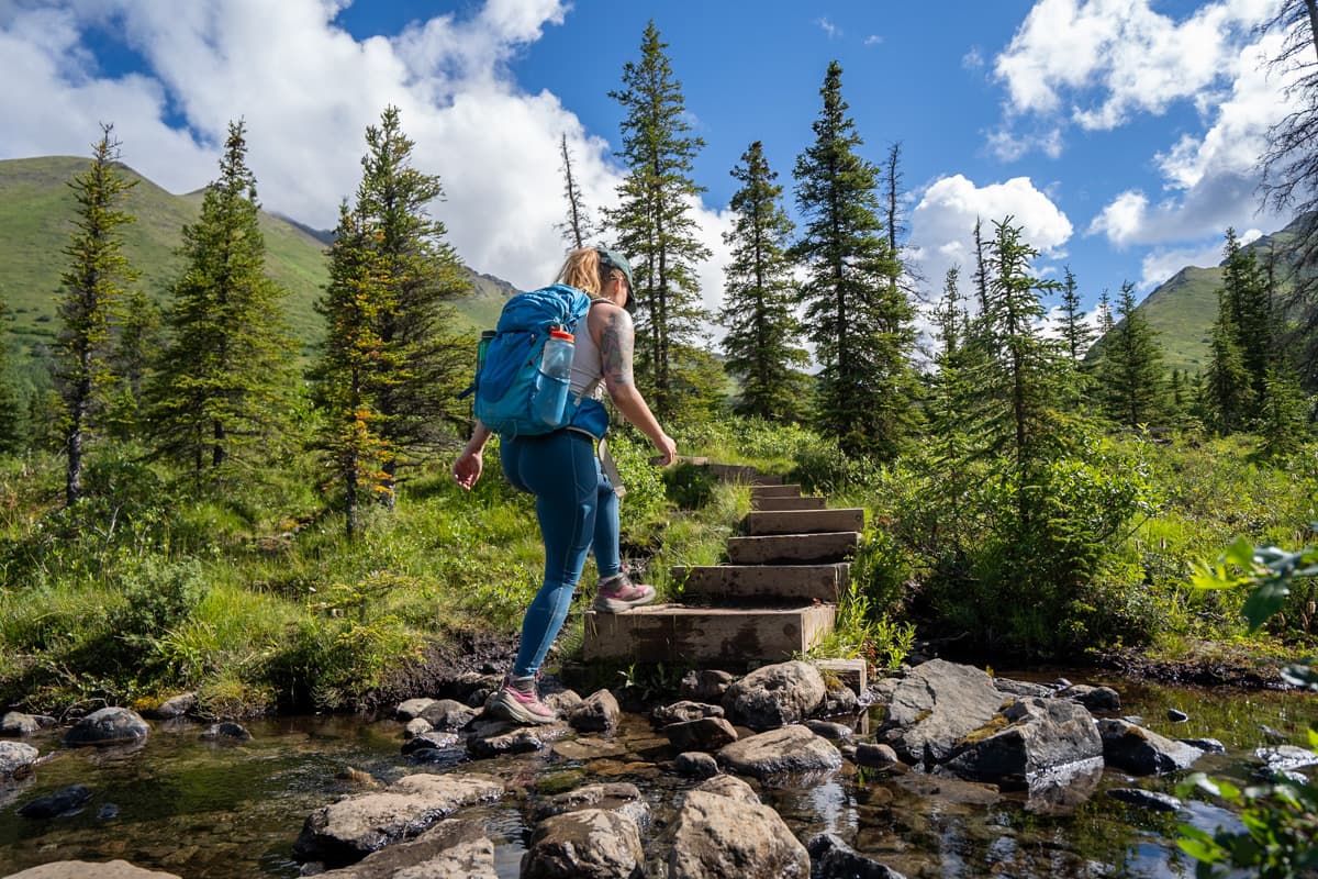 Woman hiking up stairs in a pine tree forest along the South Fork Trail in Chugach State Park, Alaska