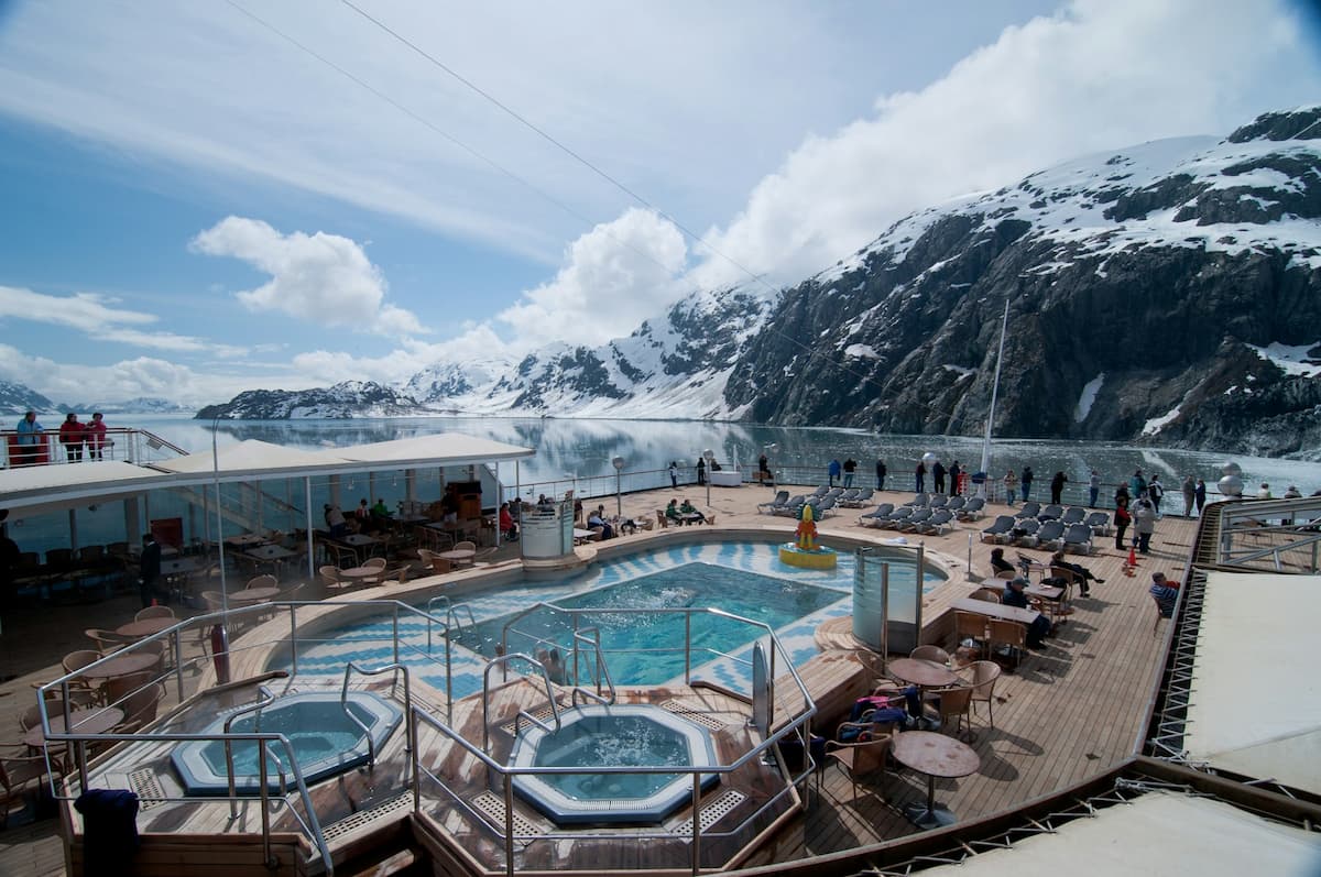 People standing on the top deck of an Alaska cruise with mountains and glaciers in the background along the Alaska coastline