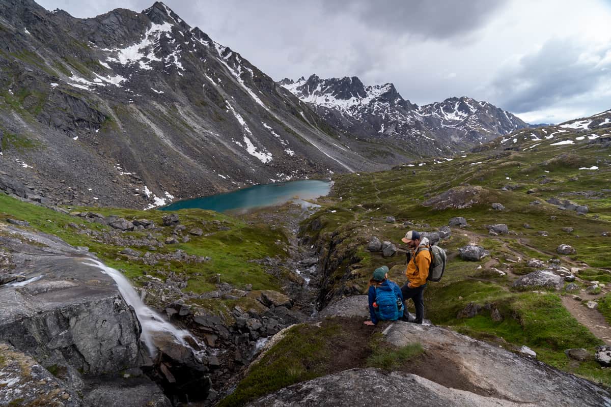 Couple standing on a rocky outcropping overlooking Reed Lake and the snowy Talkeetna Mountains along the Reed Lakes Trail in Hatcher Pass, Alaska