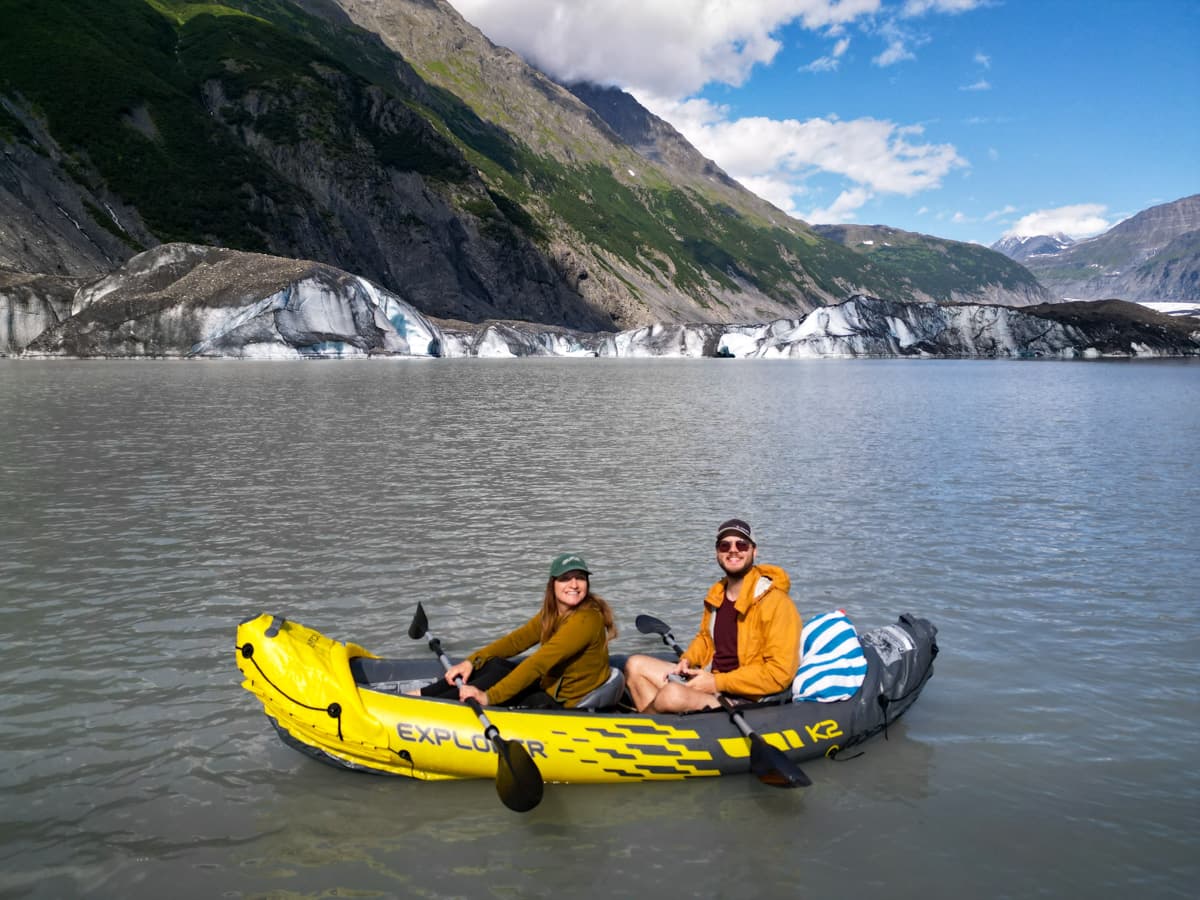 Couple sitting in an inflatable kayak with the Valdez Glacier and the Chugach Mountains in the background in Valdez, Alaska