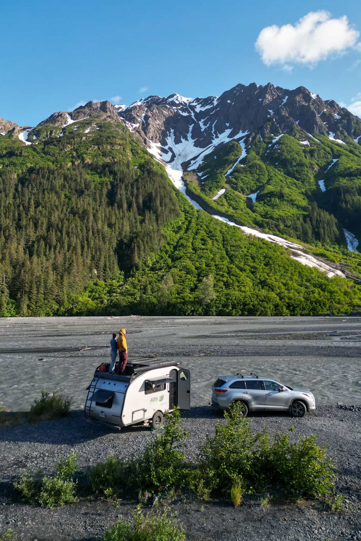 Couple standing on top of their Safari Condo Alto F1743 Expedition with a pine tree covered mountain in the background in Seward, Alaska