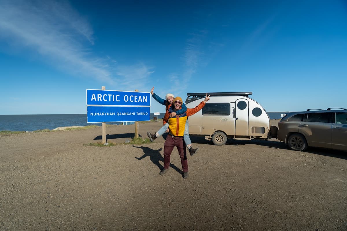 Couple standing in front of a Safari Condo Alto F1743 Expedition and the Arctic Ocean sign in Tuktoyaktuk, Northwest Territories in Canada