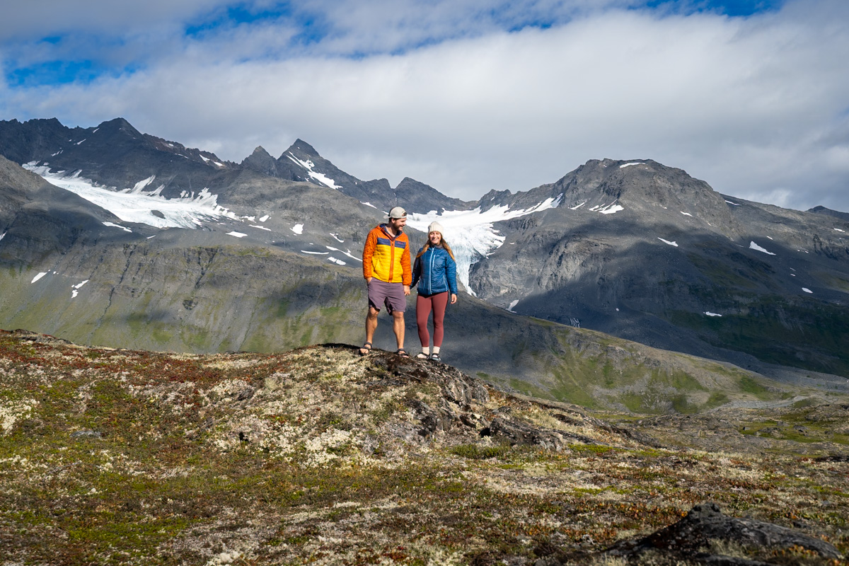Couple standing on a rocky outcropping with the Chugach Mountains in the background in Thompson Pass outside of Valdez, Alaska
