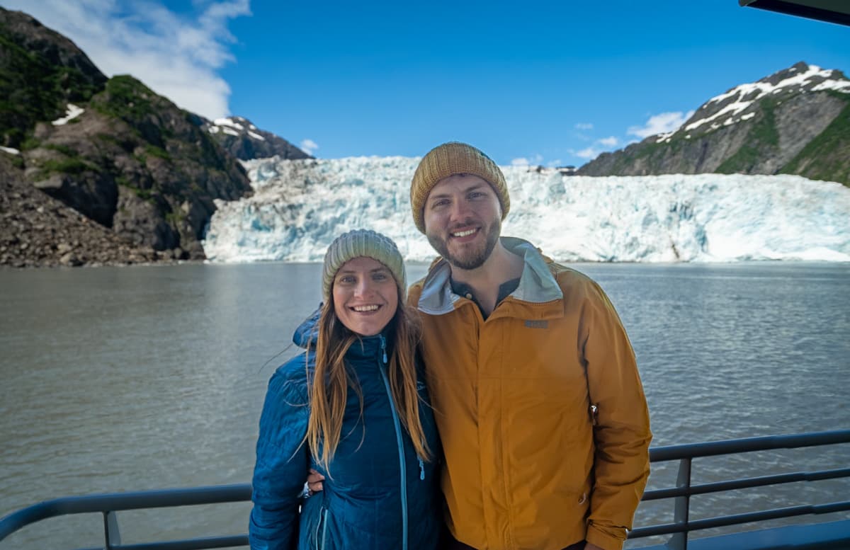 Smiling couple standing on a Major Marine cruise with a tidewater glacier in the background in Kenai Fjords National Park, Alaska