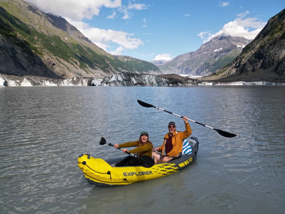 Couple sitting in an inflatable kayak with the Valdez Glacier and the Chugach Mountains in the background in Valdez, Alaska
