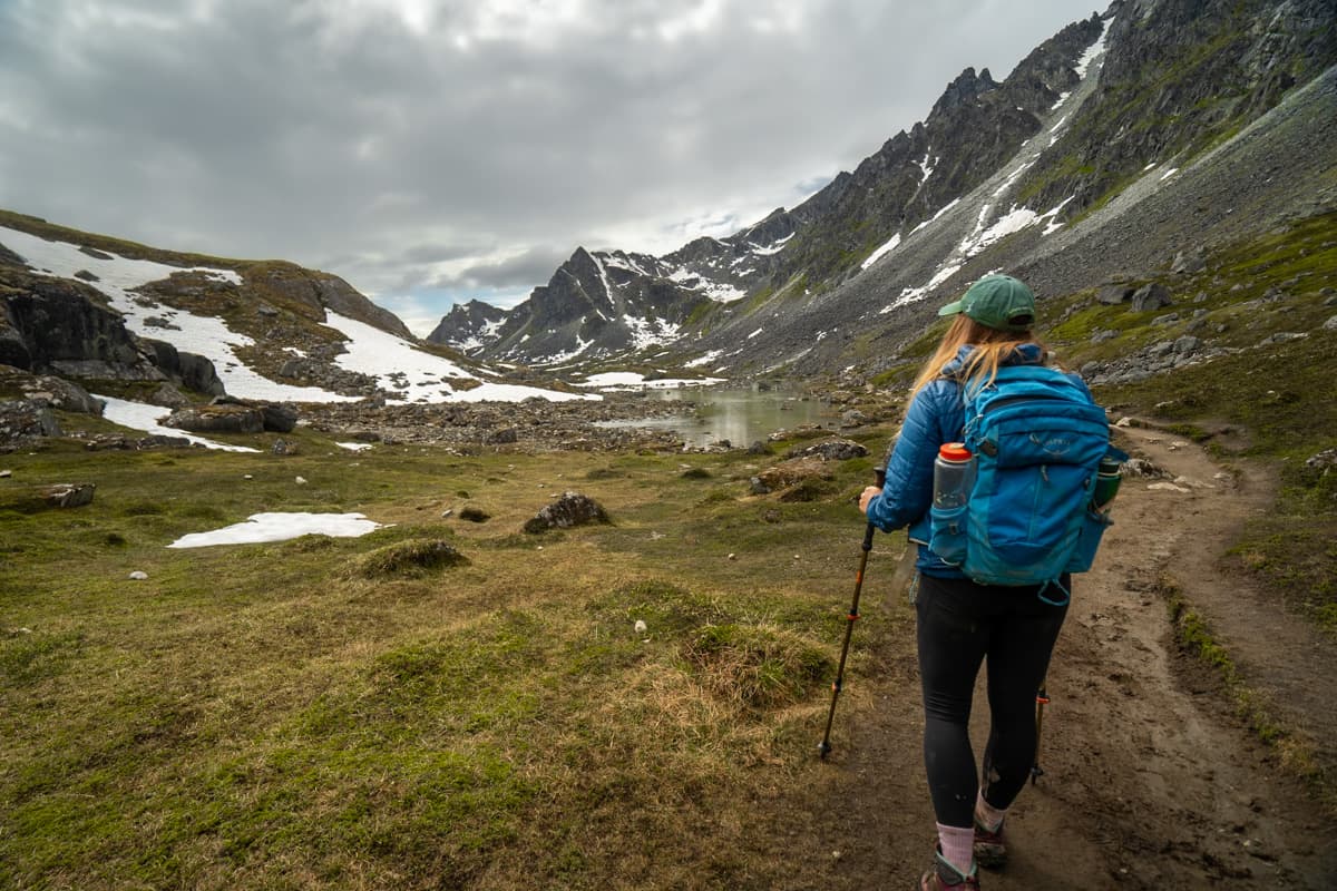 Woman with trekking poles hiking along the Reed Lakes Trail with the Talkeetna Mountains in the background in Hatcher Pass, Alaska