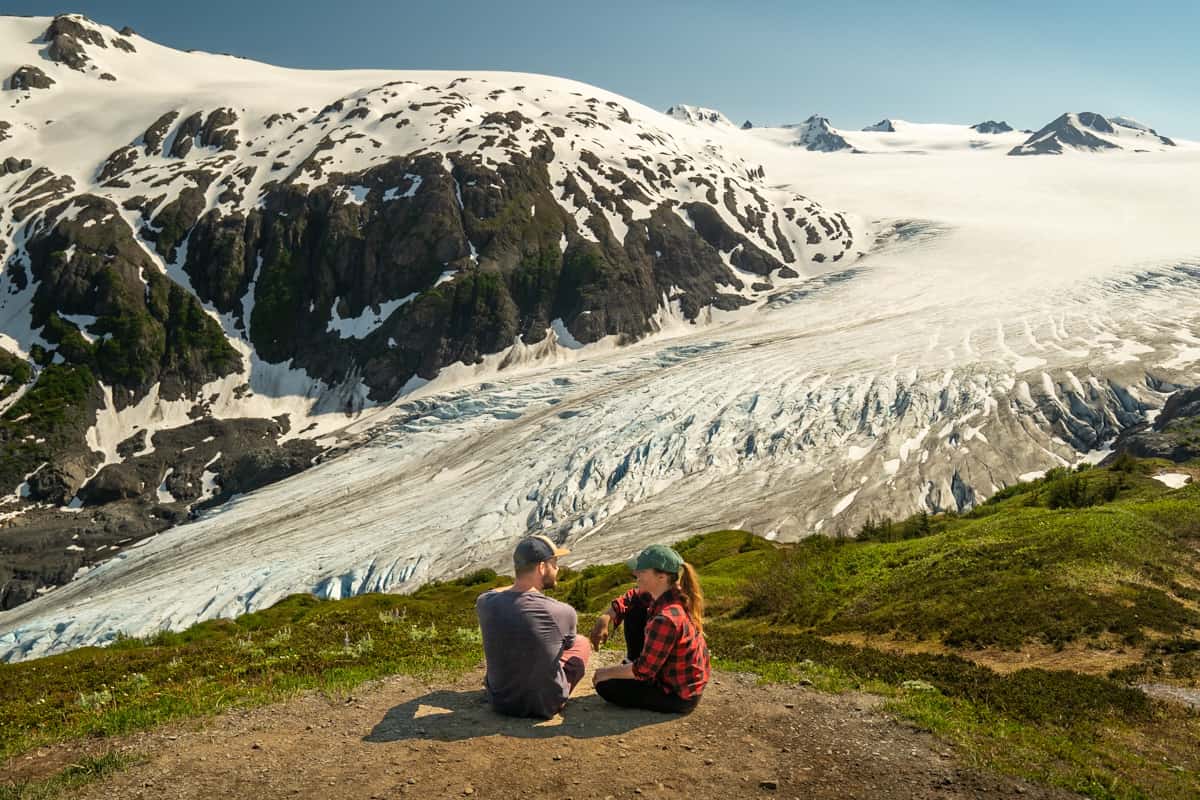 Couple sitting along a viewpoint on the Harding Icefield Trail, overlooking the Exit Glacier, in Kenai Fjords National Park in Seward, Alaska