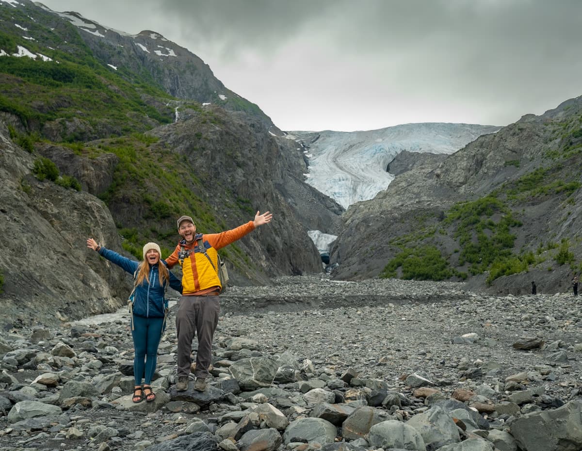 Couple standing with outstretched arms in front of the Exit Glacier along the Exit Glacier Trail in Kenai Fjords National Park in Alaska