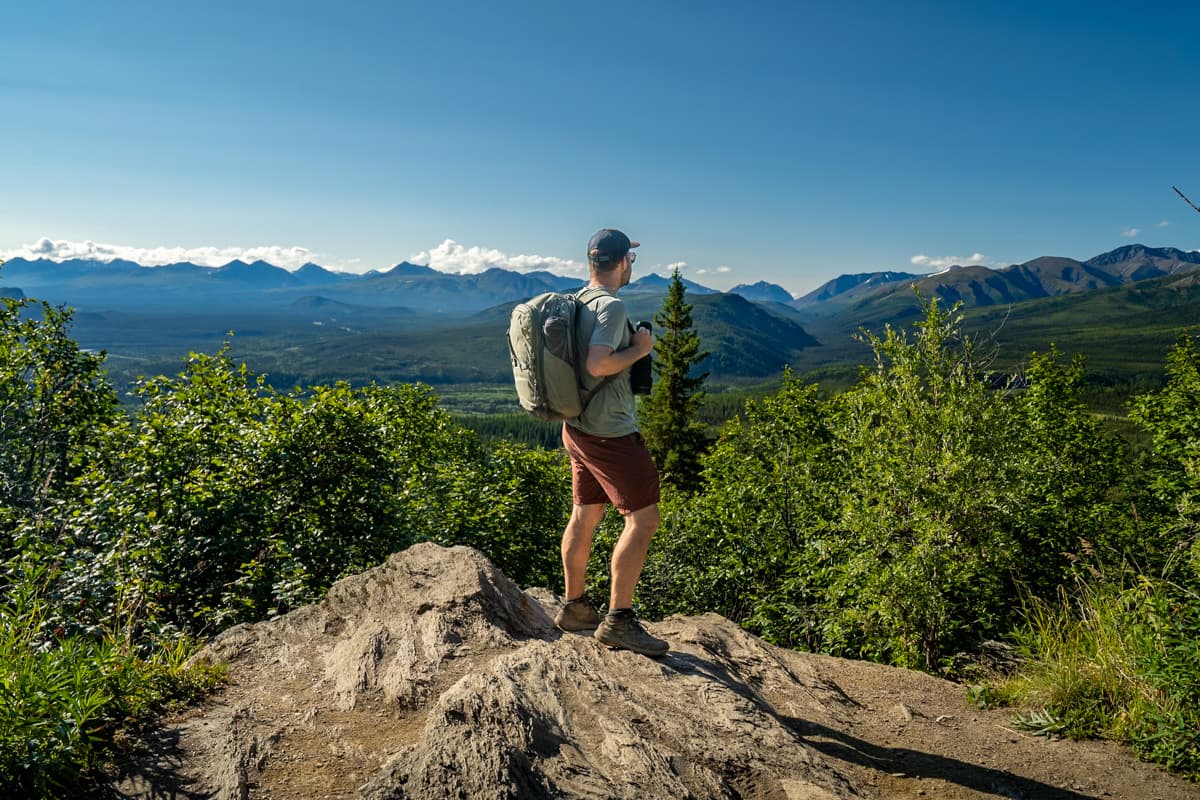 Man standing on a rocky outcropping with the Alaska Mountain range in the background along the Mount Healy Overlook Trail in Denali National Park in Alaska