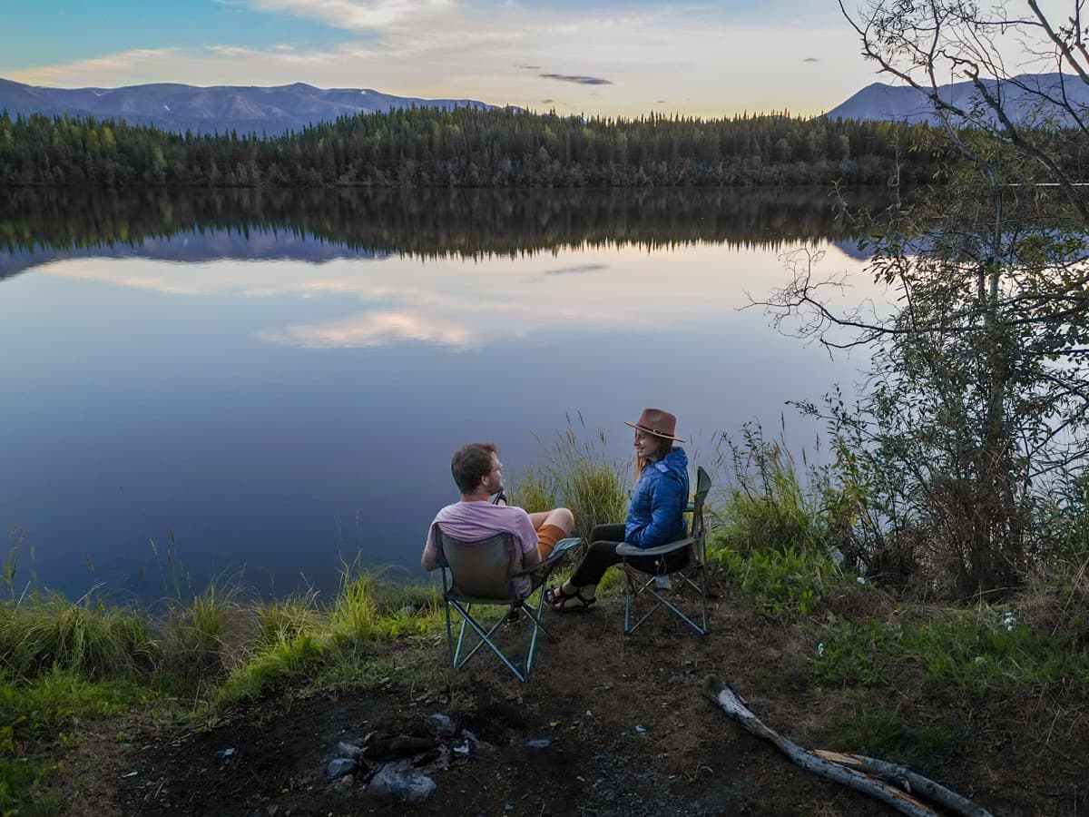 Couple sitting in camping chairs next to Moose Lake near Wrangell-St. Elias National Park near McCarthy, Alaska