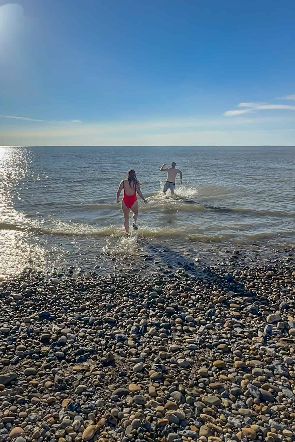 Couple running into the Arctic Ocean while wearing bathing suits in Tuktoyaktuk, Northwest Territories of Canada