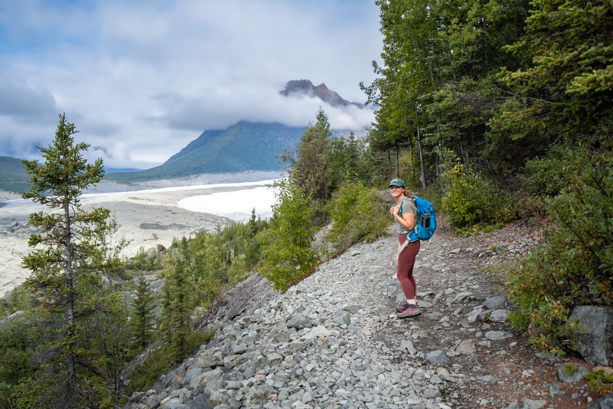 Woman hiking along a gravel trail along the Root Glacier Trail with the Root Glacier in the background in Wrangell-St. Elias National Park, Alaska