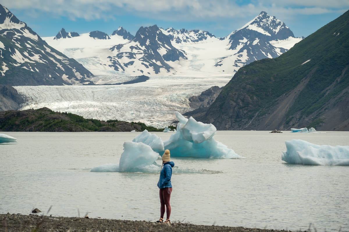 Woman standing at Grewingk Glacier lake with the Grewingk Glacier and floating icebergs in the background in Kachemak Bay State Park in Homer, Alaska