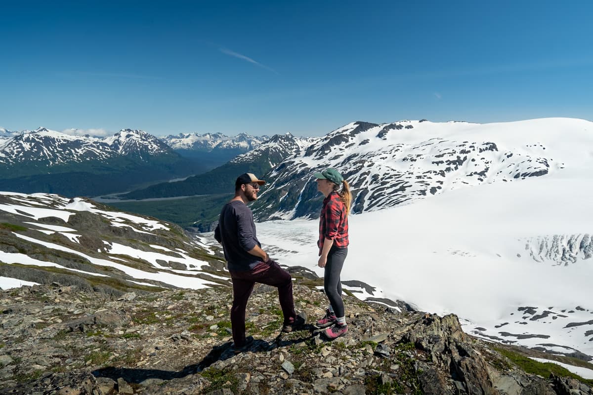 Couple standing on a rocky outcropping with the Kenai Mountains in the background along the Harding Icefield Trail in Kenai Fjords National Park in Seward, Alaska